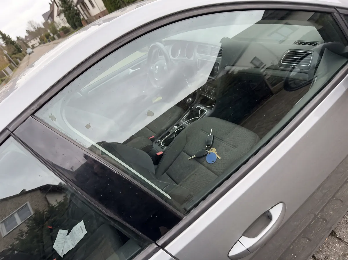 Autoschlüssel liegt auf dem Beifahrersitz eines verschlossenen silbernen Autos, durch die Seitenscheibe fotografiert